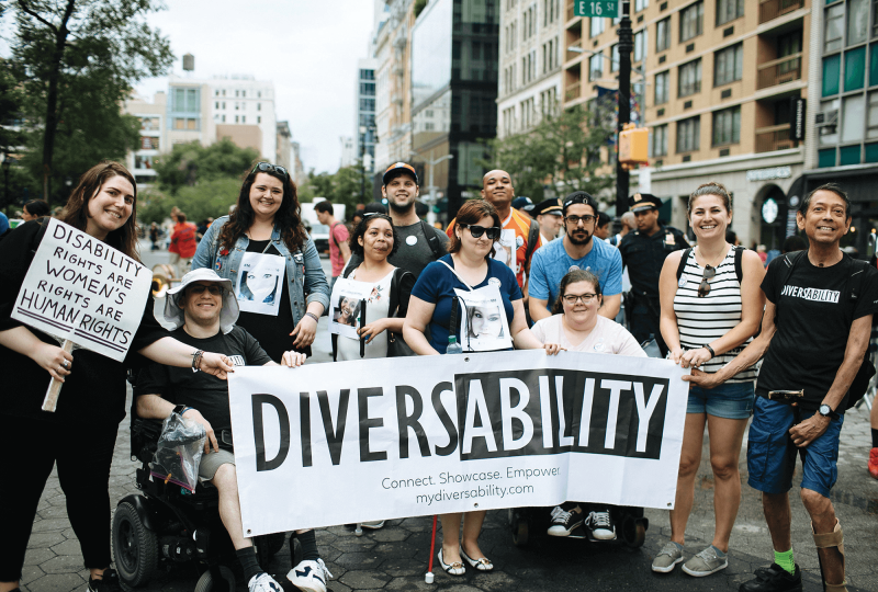 A group of smiling marchers hold a "Diversability" banner and a sign, "Disability rights are women's rights are human rights."