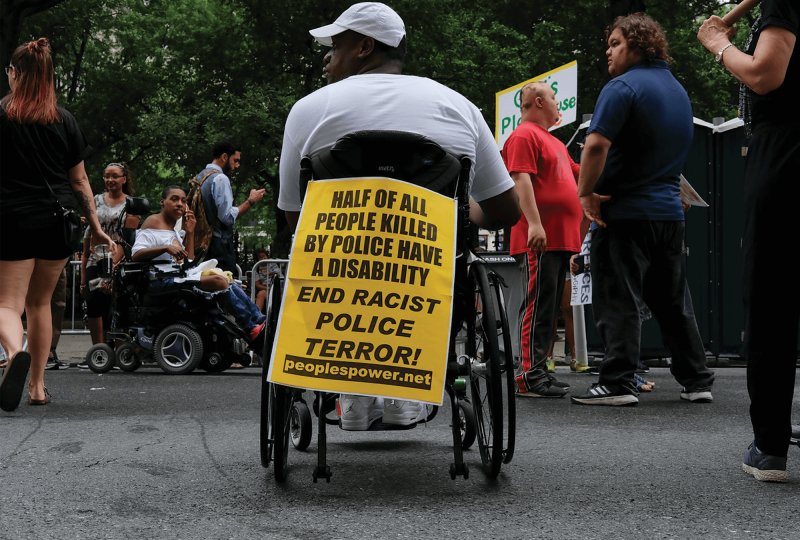 A marcher displays his sign, "Half of all people killed by police have a disability. End racist police terror." on the back of his wheelchair.