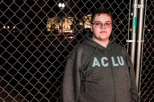 Gavin Grimm, a 17-year-old transgender boy, stands in front of a chainlink fence.