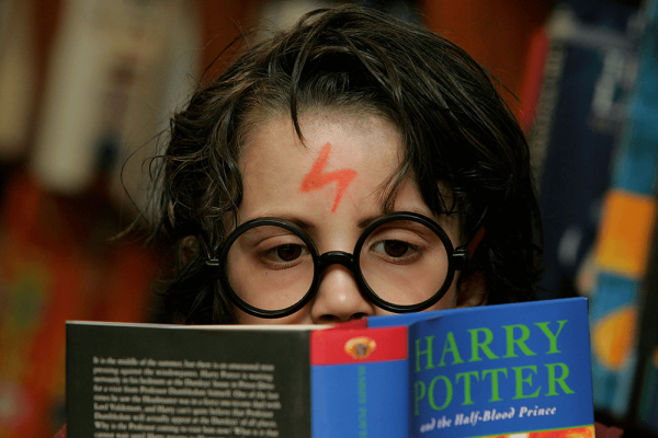 A young child reading 'Harry Potter and the half blood prince' dressed up as Harry Potter
