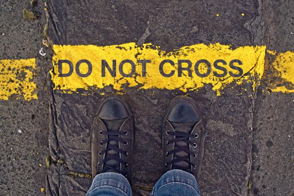 Sneakers on asphalt road and "Do Not Cross" sign. Image courtesy igor.stevanovic