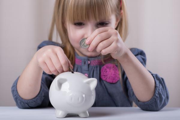 A young girl puts money in a piggy bank. Image courtesy Sofya Apkalikova/shutter