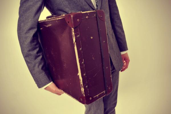 A young man carries an old suitcase. Image courtesy nito/shutterstock.com.
