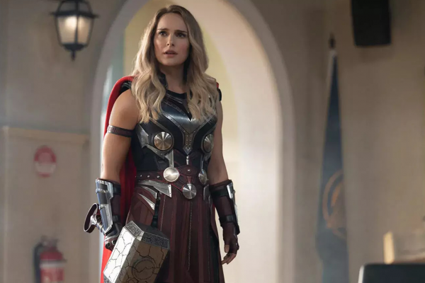Natalie Portman holds a large hammer and is dressed as Thor.