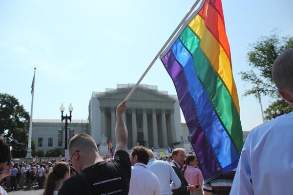 A man holds a gay pride flag in front of the Supreme Court. Image courtesy Adell