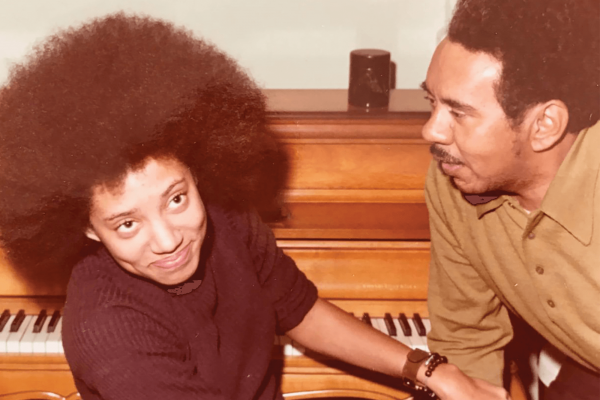 A young Nikky Finney sits at a piano with her father in 1972.