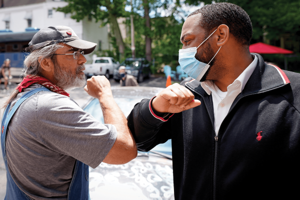 A Black man and a white man "high-fiving" each other with their elbows.