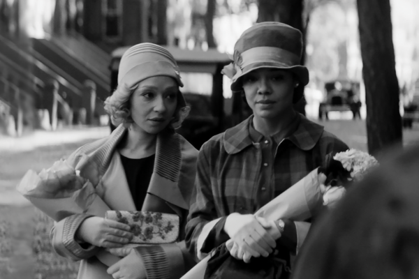 A black and white photo of two women wearing 1920s era outfits and carrying flowers