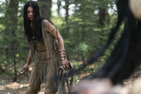 A Comanche woman stands in a combat-ready pose with a tomahawk against an assailant in the film 'Prey.'