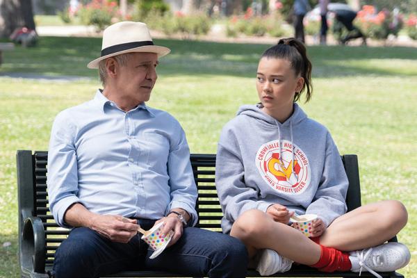 Paul (Harrison Ford) wears a light blue dress shirt and hat and sits on a black park bench next to teenage girl Alice (Lukita Maxwell), who's sitting cross-legged while wearing a gray hoodie.