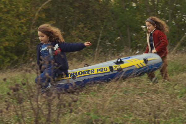Two similar-looking small girls carry a raft together through a woody path