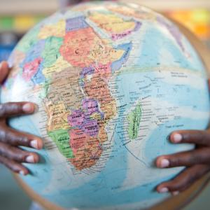 Boys hands hugging globe in classroom / Getty Images
