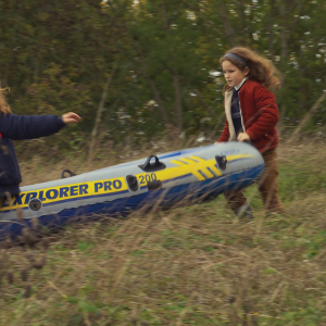 Two similar-looking small girls carry a raft together through a woody path