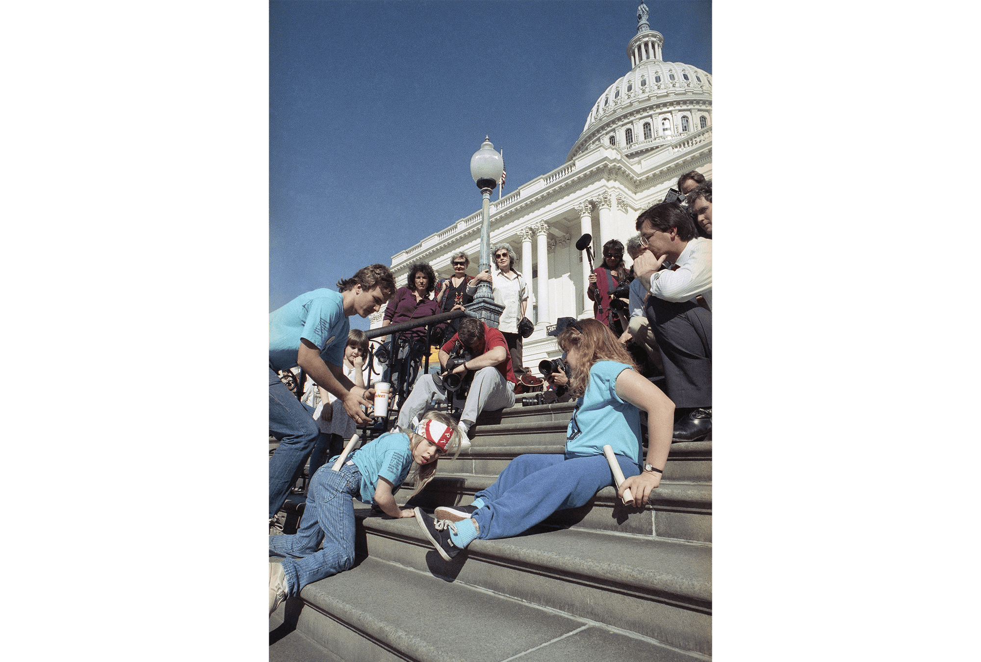 A small blond girl crawls up the Capitol steps surrounded by other crawlers, protester, and the media