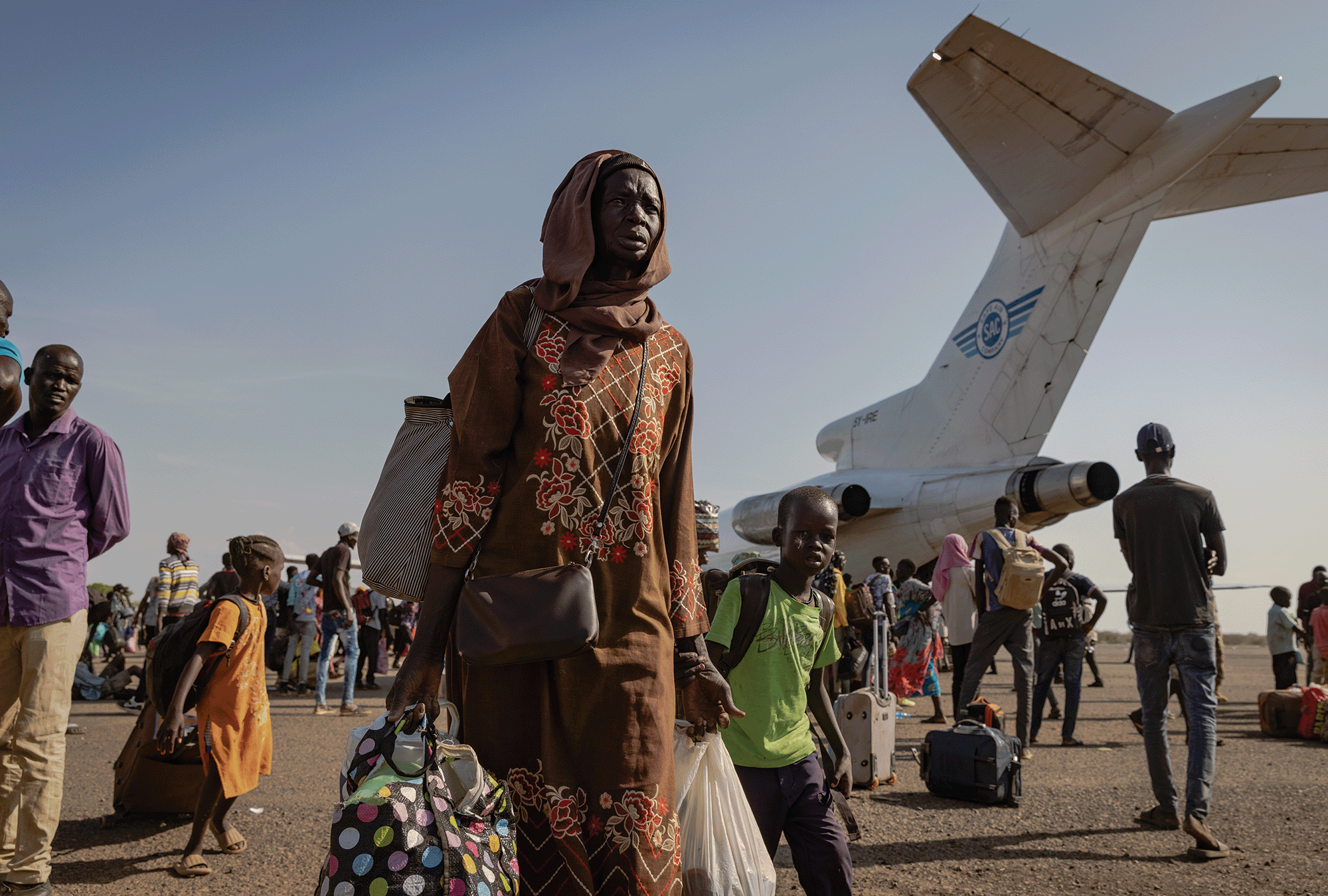 The image shows South Sudanese people boarding a government cargo plane to return home.