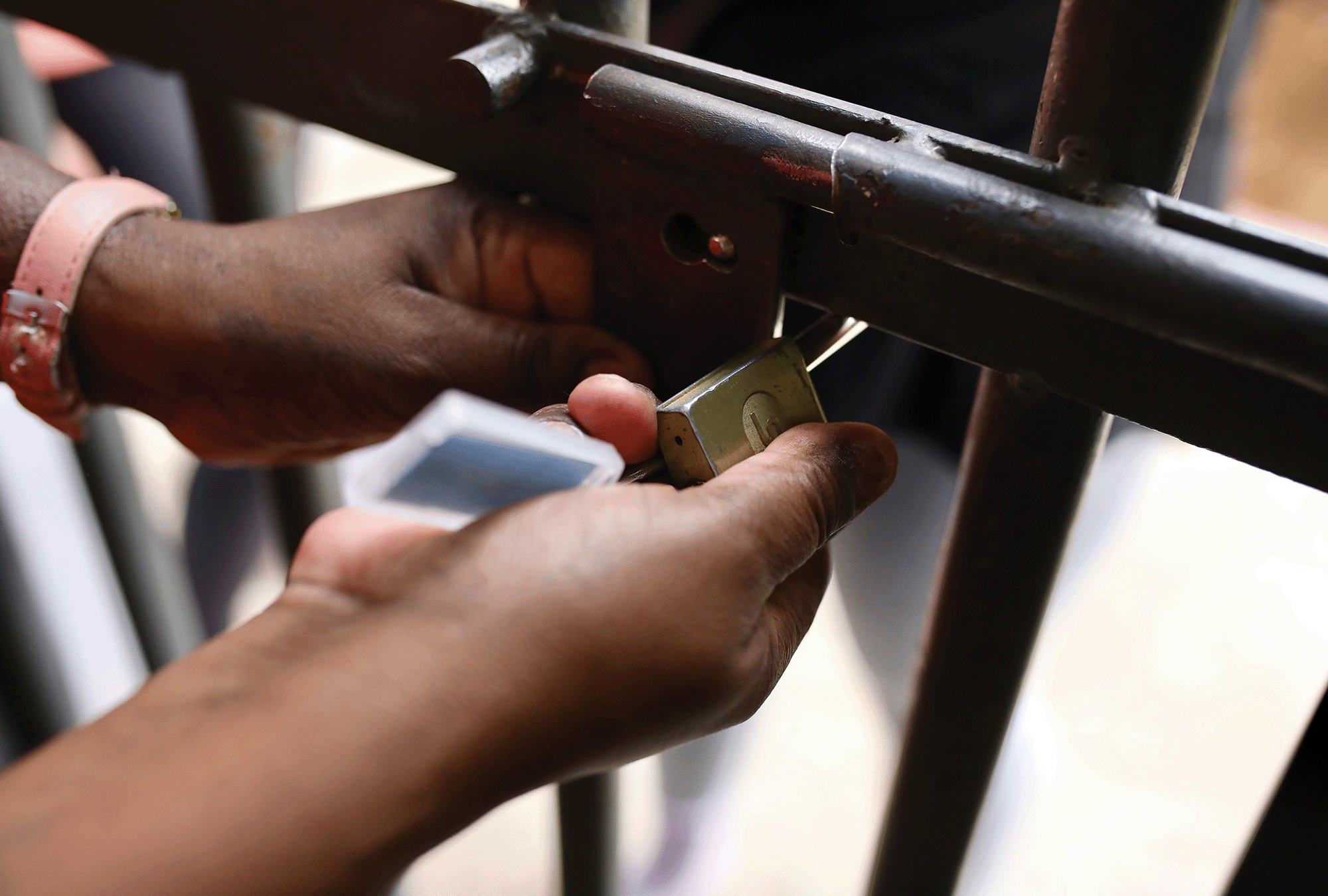 A Black person's two hands unlock a padlock on a gate 