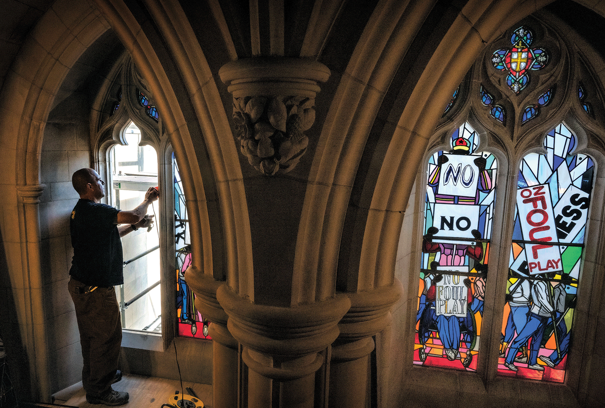 The image shows a man replacing stained glass windows in the Washington National Cathedral, the new windows depict protest scenes. 