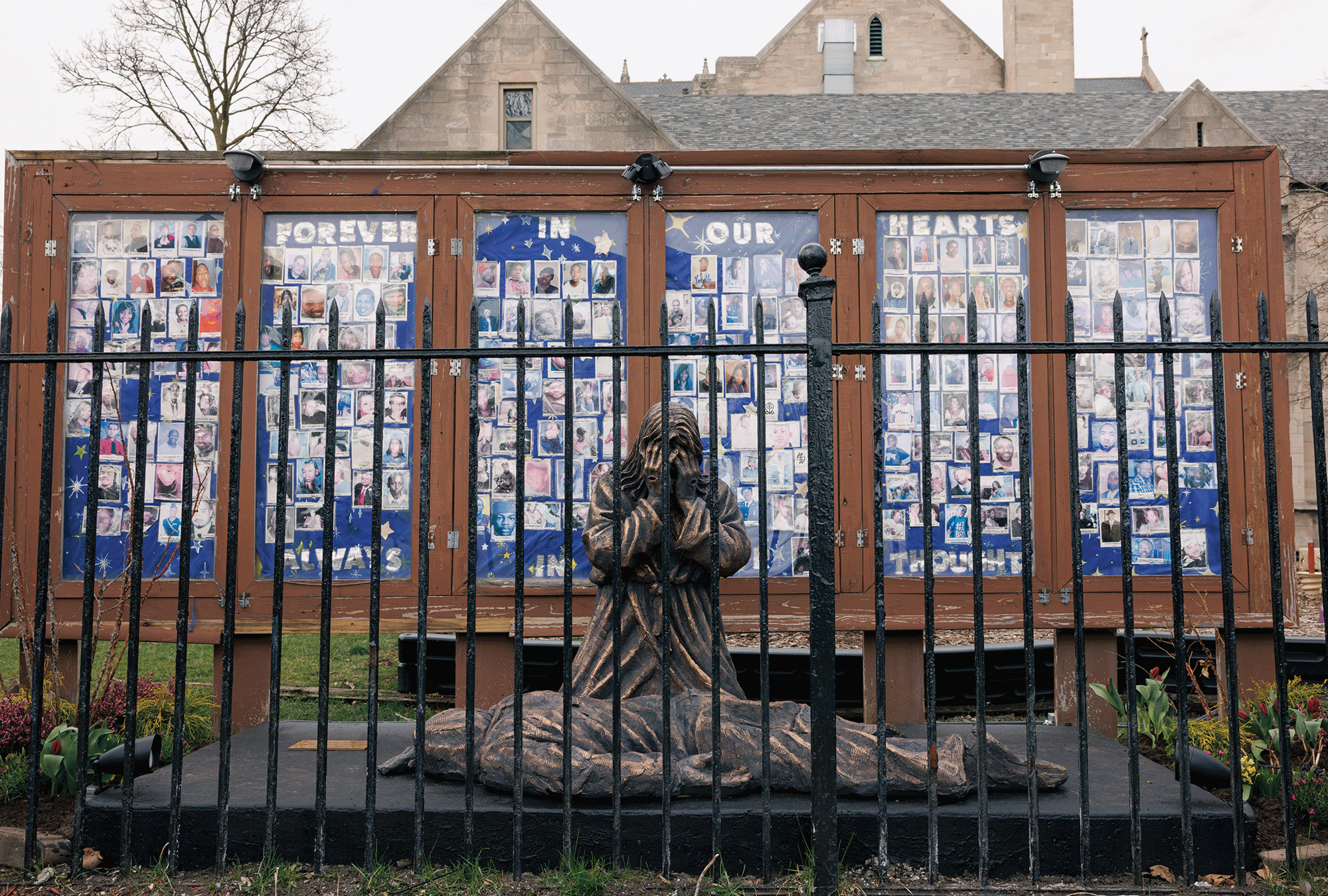 The picture shows a sculpture of a kneeling person over a body, with photos in the back of people who died of gun violence. 