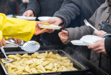 A person serves food to others waiting in line with plates.