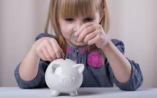 A young girl puts money in a piggy bank. Image courtesy Sofya Apkalikova/shutter