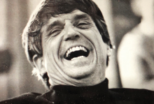 From the documentary "Seeking Shelter: A Story of Place, Faith and Resistance." A white man wearing a black turtleneck crinkles his face with exuberant laughter