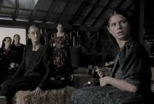 From 'Women Talking' A group of Mennonite women are standing and sitting in a barn filled with crates and hay bales in the film 'Women Talking.'