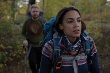 From "To the End" Foreground of image shows Rep. Alexandria Ocasio-Cortez hiking in a green forest. She wears a geometric sweater and a blue backpack; her boyfriend is pictured hiking behind her, slightly out of focus