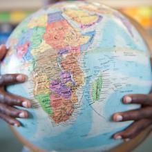 Boys hands hugging globe in classroom / Getty Images