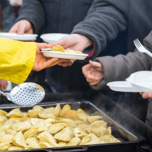 A person serves food to others waiting in line with plates.
