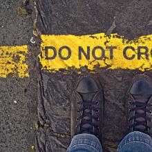 Sneakers on asphalt road and "Do Not Cross" sign. Image courtesy igor.stevanovic