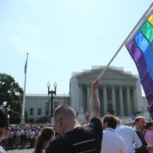 A man holds a gay pride flag in front of the Supreme Court. Photo via Adelle M. 