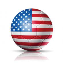 An illustration of a soccer ball with an American flag all over its surface. It's on the ground of a completely white background.
