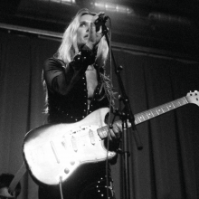 Black and white photo of Natalie Bergman holding an electric guitar and singing into a mic stand