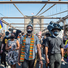 Jumaane Williams walks in front of a group of masked Black people crossing the Brooklyn Bridge