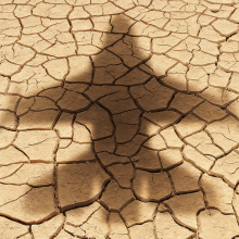The shadow of a military aircraft falls over parched, cracked land
