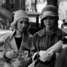 A black and white photo of two women wearing 1920s era outfits and carrying flowers