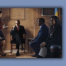 A scene from Philly DA of Larry Krasner sitting in a chair.