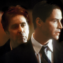 The image shows a scene from "The Devil's Advocate," where one white man is looking over the shoulder of another white man in a suit, who is looking out a window. 
