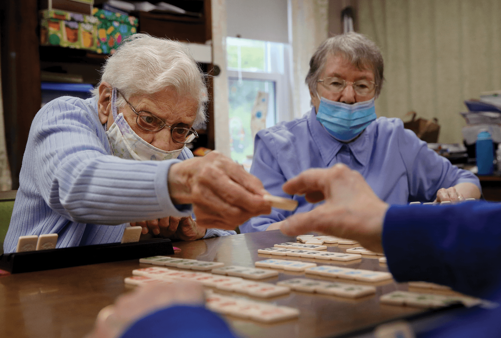 Sister Gloria Cote and Sister Claire Robert at St. Chretienne retirement home in Marlborough, Mass. / Craig F. Walker / The Boston Globe Three Felician Catholic sisters play a board game together, all wearing masks.