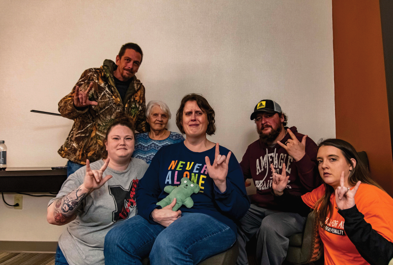 The image shows six people holding up the sign language for "I love you" 