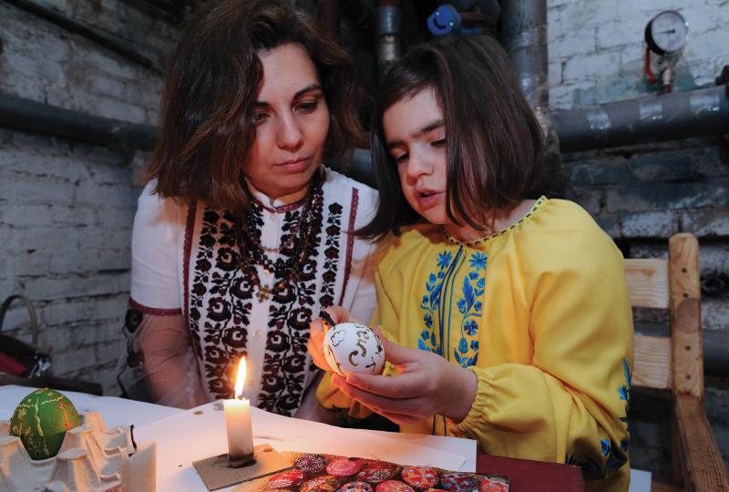 A Ukrainian woman and girl are sitting together as they paint an Easter egg.