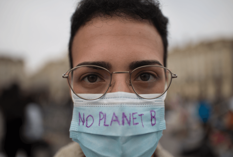 A young adult with dark hair and glasses is wearing a mask with the words "No Planet B" written on it.