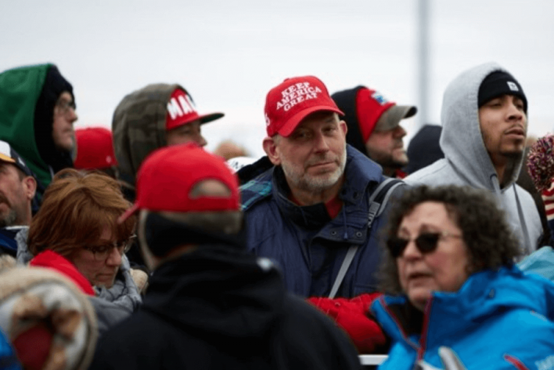 Crowd of people and image is focused on man wearing a "Make America Great Again" hat. 