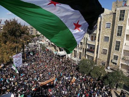 Syria independence flag flies over a large pathering of protesters in Idlib. Photo courtesy FreedomHouse via Flickr Photo courtesy FreedomHouse via Flickr