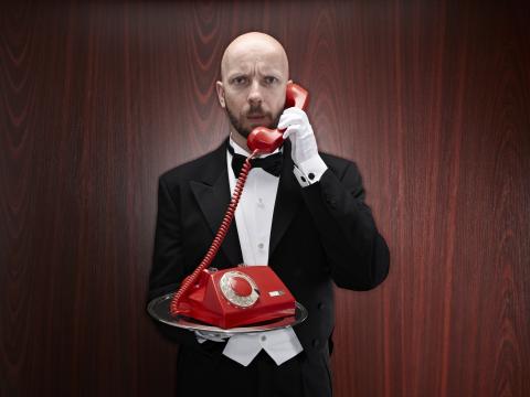 Butler with a red telepfone on a silver tray. Photo via Getty Images. Butler with a red telepfone on a silver tray. Photo via Getty Images.