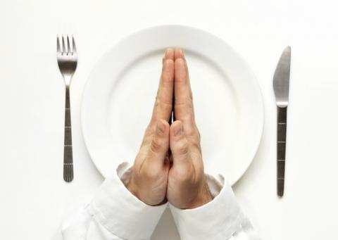 Man praying over a white plate while awaiting to be fed. Photo courtesy Marcell Mizik/Shutterstock.com. Photo courtesy Marcell Mizik/Shutterstock.com.