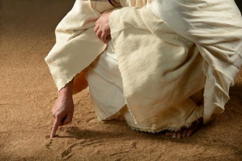 Jesus writes in the sand with his finger.