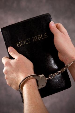 Handcuffed male hands hold a black Holy Bible. Steven Frame / Shutterstock Steven Frame / Shutterstock
