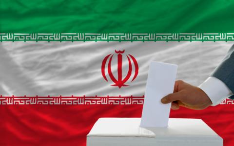 A man casts his vote in front of the flag of Iran. Photo courtesy Vepar5/shutterstock.com