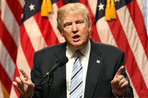 Trump speaks to a gathered audience before an American flag backdrop.